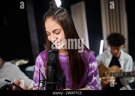 simpatica ragazza adolescente che canta e guarda il telefono cellulare accanto ai suoi amici Foto Stock