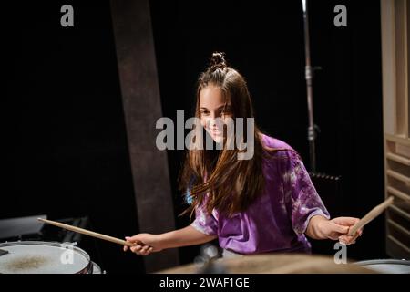 allegro e adorabile adolescente di talento con un vivace vestito di tutti i giorni che suona la chitarra e sorride felicemente Foto Stock