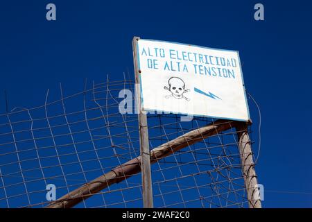 Peligro / segnale di pericolo in spagnolo avvertimento di cavi elettrici ad alta tensione sulla diga di scarico dei residui di scarto dalle miniere vicine alla periferia di Potosi, Bolivia Foto Stock