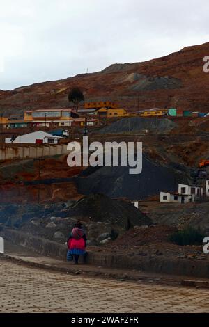 Donna Quechua locale che indossa abiti tradizionali cammina lungo la strada alla base di Cerro Rico, passando accanto a una miniera cooperativa nelle vicinanze, Potosi, Bolivia Foto Stock