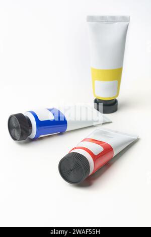 tubi di pittura dell'artista sparsi con cappuccio nero isolato su sfondo bianco, forniture artistiche di colori primari blu, giallo e rosso, modello modello di mock-up Foto Stock