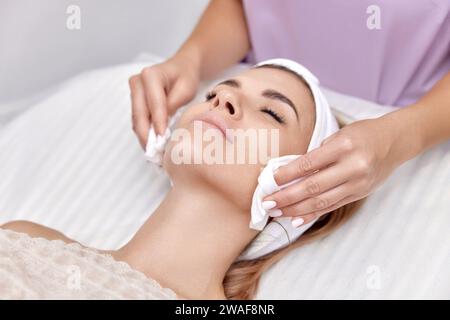 estetista pulisce la pelle di bella donna con spugna. Pulizia perfetta, trattamento spa viso skincare. Foto Stock