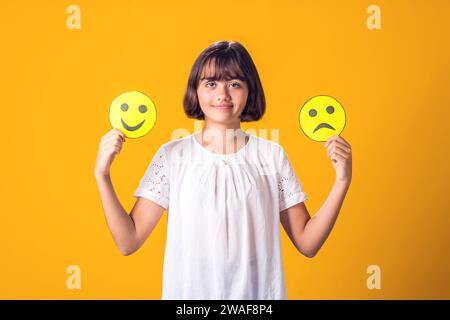 La ragazza tiene in mano emoticon tristi e felici. Concetto di salute mentale, psicologia ed emozioni dei bambini Foto Stock