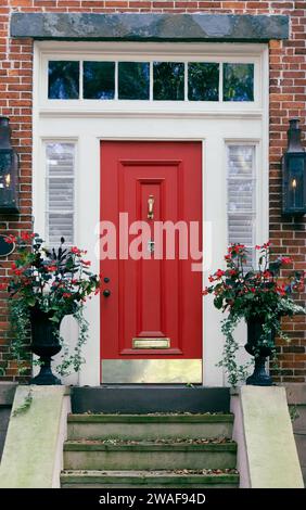 Una porta frontale di colore rosso brillante con finiture color crema e uno specchio di poppa con gradini frontali su un edificio di mattoni rossi Foto Stock