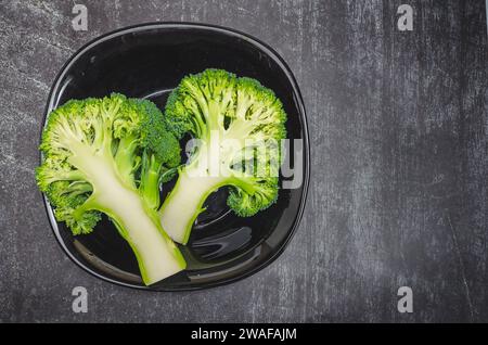 Due metà di broccoli verdi freschi in un recipiente nero su sfondo grigio. Una dieta sana. Foto Stock