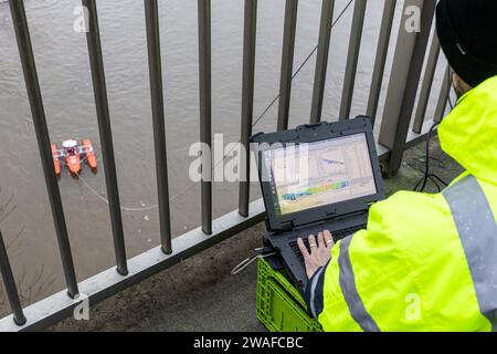 4 gennaio 2024, Assia, Gießen: I dipendenti delle vie navigabili e dell'ufficio spedizioni Mosel-Saar-Lahn monitorano lo scarico delle inondazioni dal ponte di Sachsenhausen utilizzando un flussometro a profilo Doppler a ultrasuoni. Foto: Christian Lademann/dpa Foto Stock