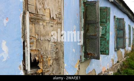 vista della facciata di una vecchia casa abbandonata con finestre inondate e ricoperte di compensato e persiane in una prospettiva che si ritira Foto Stock