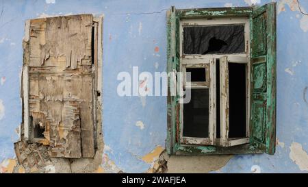 frammento della facciata di un vecchio edificio fatiscente con una finestra a vetri aperti e una finestra rivestita di compensato Foto Stock