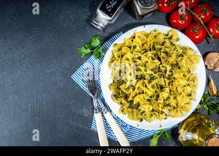 Pranzo italiano mediterraneo. Farfalle con spinaci, funghi, verdure e salsa cremosa. Su tavolo nero in calcestruzzo, con spezie per din Foto Stock
