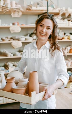 Una donna vasaio tiene una scatola con prodotti di argilla cruda Foto Stock