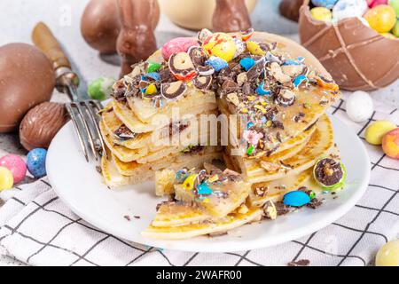 La colazione per i bambini è divertente e carina per Pasqua. Frittelle americane, torte fritte con uova di cioccolato pasquale, marshmallows, farcitura di zucchero con rotto Foto Stock