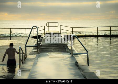 Un uomo in piedi nelle acque poco profonde di un oceano vicino a un molo Foto Stock