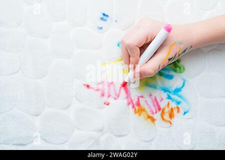 La mano di un bambino disegna penne in feltro sui mobili imbottiti bianchi del divano o di un tappeto. vista dall'alto. Macchia sporca per il concetto di pulizia Foto Stock