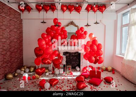 Arredamento elegante per San Valentino. Caminetto vicino a parete bianca decorato con palloncini rossi a forma di cuore, regali a pavimento in scatole per le vacanze, borse, ecc. Foto Stock