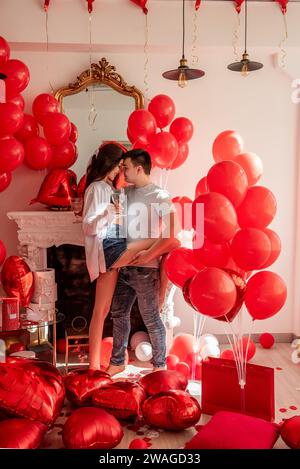 Un momento di gioia tra la danza di giovani coppie che festeggiano con un brindisi di San Valentino vicino a palloncini rossi. Donna che regge un bicchiere di vino, occhi coperti, uomo abbraccia, Foto Stock