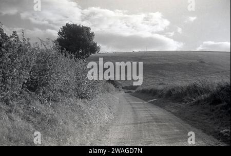 Anni '1950, storica, stretta strada di campagna tra i campi delle colline di Shropshire, Inghilterra, Regno Unito. Foto Stock