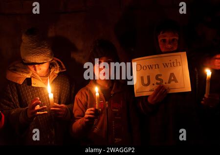 I musulmani sciiti del Kashmir tengono candele e un cartello con la scritta ''Down with USA'' durante una veglia a lume di candela. Nella periferia di Srinagar, Kashmir, i musulmani sciiti della comunità del Kashmir hanno tenuto una veglia a lume di candela esprimendo la loro opposizione a Israele e agli Stati Uniti. Il solenne raduno ha avuto una svolta tragica, in quanto 84 persone hanno perso la vita e numerosi altri hanno riportato ferite in un'esplosione durante una cerimonia commemorativa della morte del generale iraniano Qassem Soleimani. Lo Stato islamico ha rivendicato la responsabilità delle due esplosioni distruttive che hanno causato la morte di 84 persone durante il corso Foto Stock