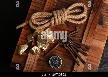 Scatola di legno con attrezzatura da viaggio e pepite dorate su sfondo nero Foto Stock