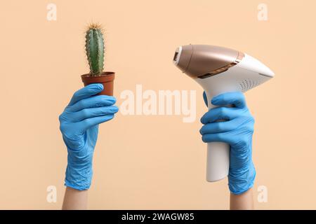 Mani femminili in guanti di gomma con cactus e moderno fotoepilatore su sfondo colorato, primo piano Foto Stock