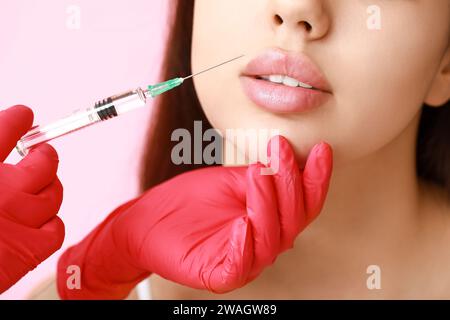 Bella giovane donna che riceve l'iniezione delle labbra su sfondo rosa, primo piano Foto Stock