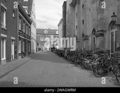 Maastricht, il centro città dei Paesi Bassi con vecchi edifici storici, negozi, negozi con biciclette parcheggiate in fila su una strada acciottolata in B&W. Foto Stock