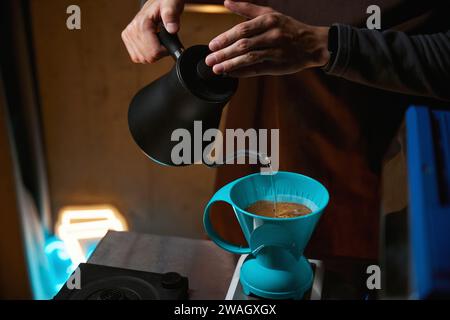 Il barista versa acqua sui chicchi di caffè macinati contenuti nel filtro Foto Stock