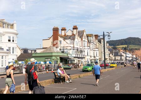 Sidmouth, Devon, Inghilterra, gente che cammina lungo la spianata in un caldo giorno del 2023 settembre, con vedute della costa giurassica di arenaria rossa e dei caffè degli hotel Foto Stock