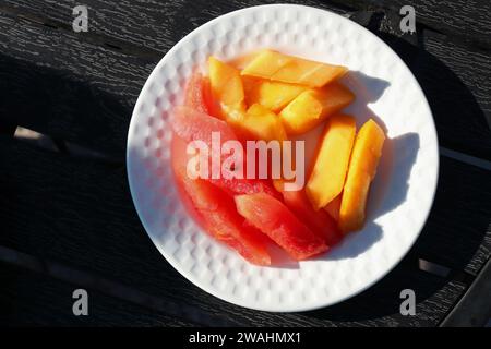 Bellissimi frutti a fette in un piatto bianco su un tavolo di legno. frutta sana, cocomero e papaia. copia spazio. Vassoio di frutta. Concetto di digiuno. Foto Stock
