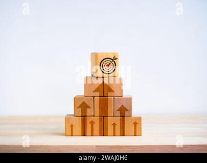 L'icona target sopra i blocchi cubi in legno si accumula come forma piramidale con frecce verso l'alto su sfondo bianco. Processo degli obiettivi aziendali, Growth Marketing, prof Foto Stock