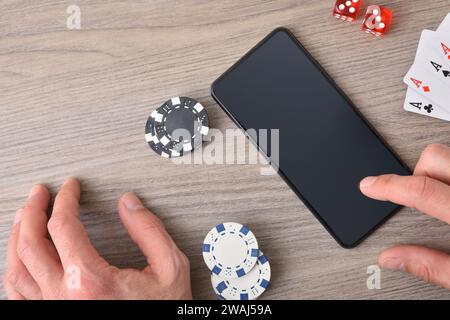 Concetto di gioco d'azzardo online con la mano utilizzando lo smartphone su un tavolo di legno e pezzi di gioco. Vista dall'alto. Foto Stock