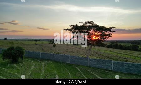 Un idilliaco paesaggio rurale caratterizzato da un cielo colorato al tramonto con sagome di alberi e una recinzione in primo piano Foto Stock