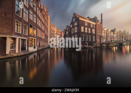 Il tramonto proietta un caldo bagliore sui tranquilli canali di Amsterdam, con gli storici edifici olandesi riflessi nell'acqua Foto Stock