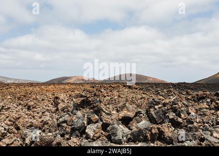Rocce di lava frastagliate si estendono in primo piano con dolci colline vulcaniche sotto un cielo nuvoloso nel paesaggio di Lanzarote Foto Stock