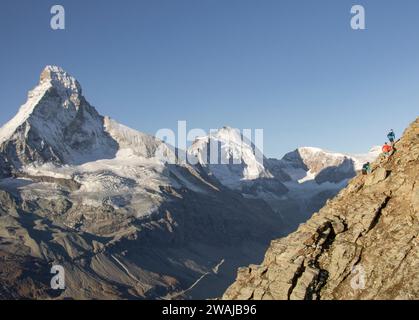Vista posteriore di tre alpinisti anonimi che salgono su un ripido pendio roccioso con l'imponente monte Cervino che si staglia sullo sfondo sotto una limpida sk Foto Stock