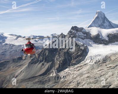 Un elicottero di soccorso rosso che vola in primo piano con la montagna innevata del Cervino sulle Alpi svizzere sullo sfondo Foto Stock