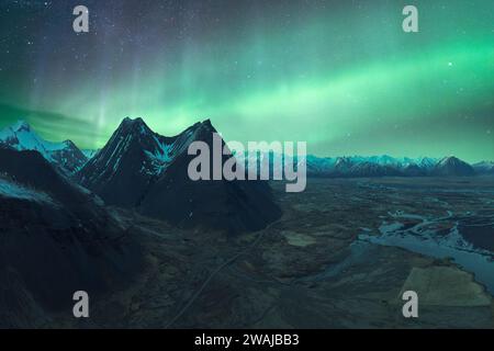 Maestose cime montuose sotto il bagliore verde dell'aurora boreale nel Parco Nazionale Vatnajokull, Islanda Foto Stock