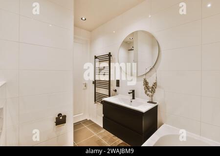 Specchio rotondo sul lavandino e armadio nero montato su pareti piastrellate nello spazioso bagno del moderno appartamento Foto Stock