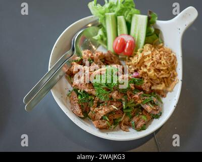 Street food tailandese. Insalata di maiale alla griglia, carne di maiale alla griglia con carbone e fette (Moo Nam Tok). Foto Stock