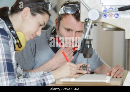 uomo che supervisiona una giovane donna usando un trapano da banco Foto Stock