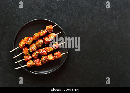 Spiedini di pollo Teriyaki su piatto su sfondo nero. Vista dall'alto, base piatta Foto Stock