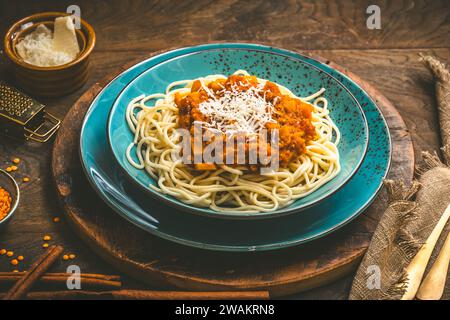 Spaghetti con salsa vegan alla bolognese fatta in casa a base di lenticchie rosse e zucca su fondo di legno, terracotta turchese Foto Stock