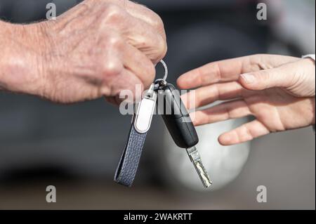 Un uomo d'affari consegna a una donna la chiave di un'auto davanti a un'auto sfocata Foto Stock