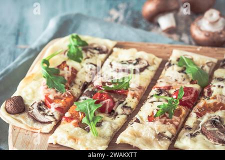 Flammkuchen appena sfornato, tradizionale flambee francese tarte o pizza tedesca in una ricetta vegetariana con funghi, formaggio spalmabile, pomodori e rucola, Foto Stock