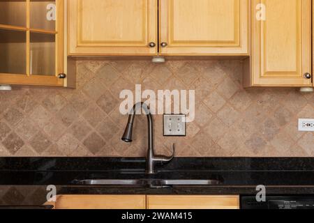 Un dettaglio della cucina con armadietti in legno, un backsplash di piastrelle in pietra quadrata e ripiano in marmo nero. Foto Stock