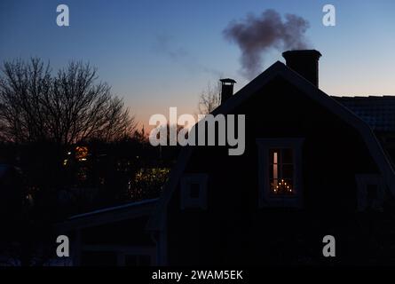 Clima stagionale, qualcuno che brucia nella stufa a legna in una casa, fumo dal camino è visibile nel cielo con il freddo. Foto Stock