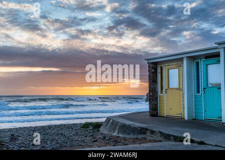 Tramonto su una spiaggia con capanne colorate a Bude, Cornovaglia, Inghilterra, Regno Unito Foto Stock