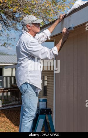 Uomo anziano, 80 anni, che lavora su una scala che dipinge il rivestimento su una casa, USA. Foto Stock