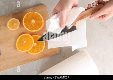 Donna che pulisce il coltello con un tovagliolo di carta al tavolo, vista dall'alto Foto Stock