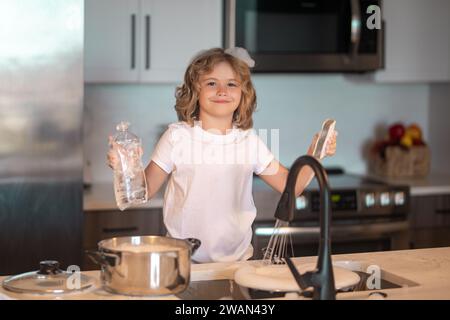 Simpatici ragazzi gemelli che aiutano in cucina con il lavaggio dei piatti. I bambini si divertono con i lavori di casa. I bambini lavano i piatti nell'interno della cucina. Bambino Foto Stock