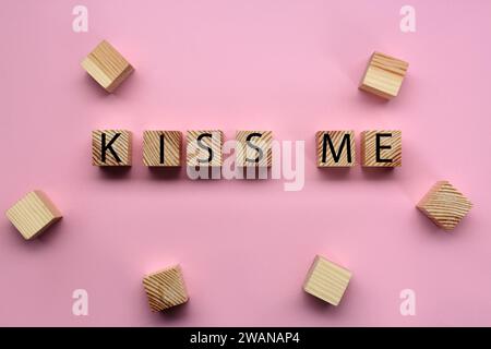 Cubi di legno con frase Kiss me su sfondo rosa, piatto Foto Stock